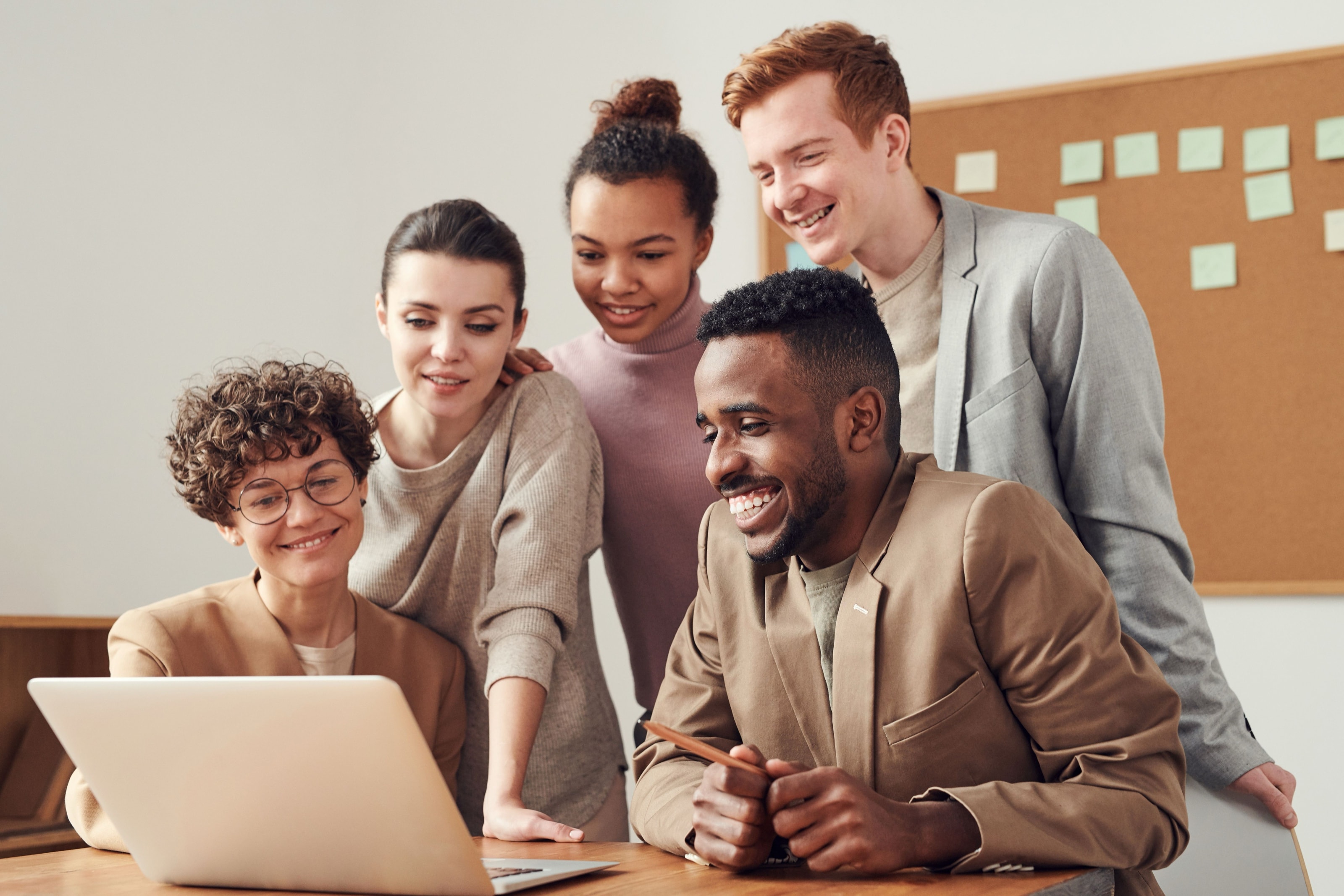 Cinque persone collaborano intorno a un laptop, sorridendo
