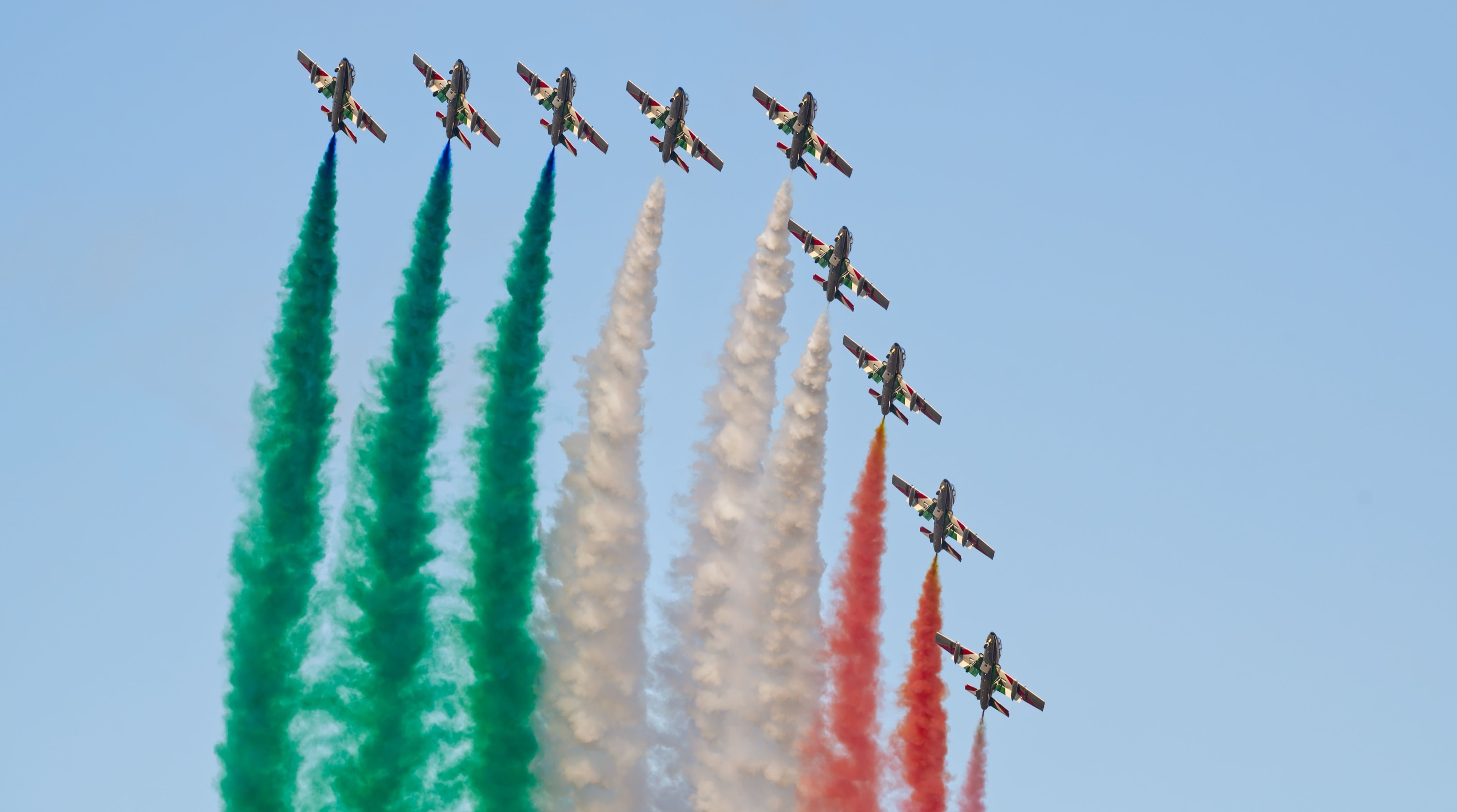 Le Frecce Tricolori in formazione, con le scie verde, bianca e rossa su cielo azzurro