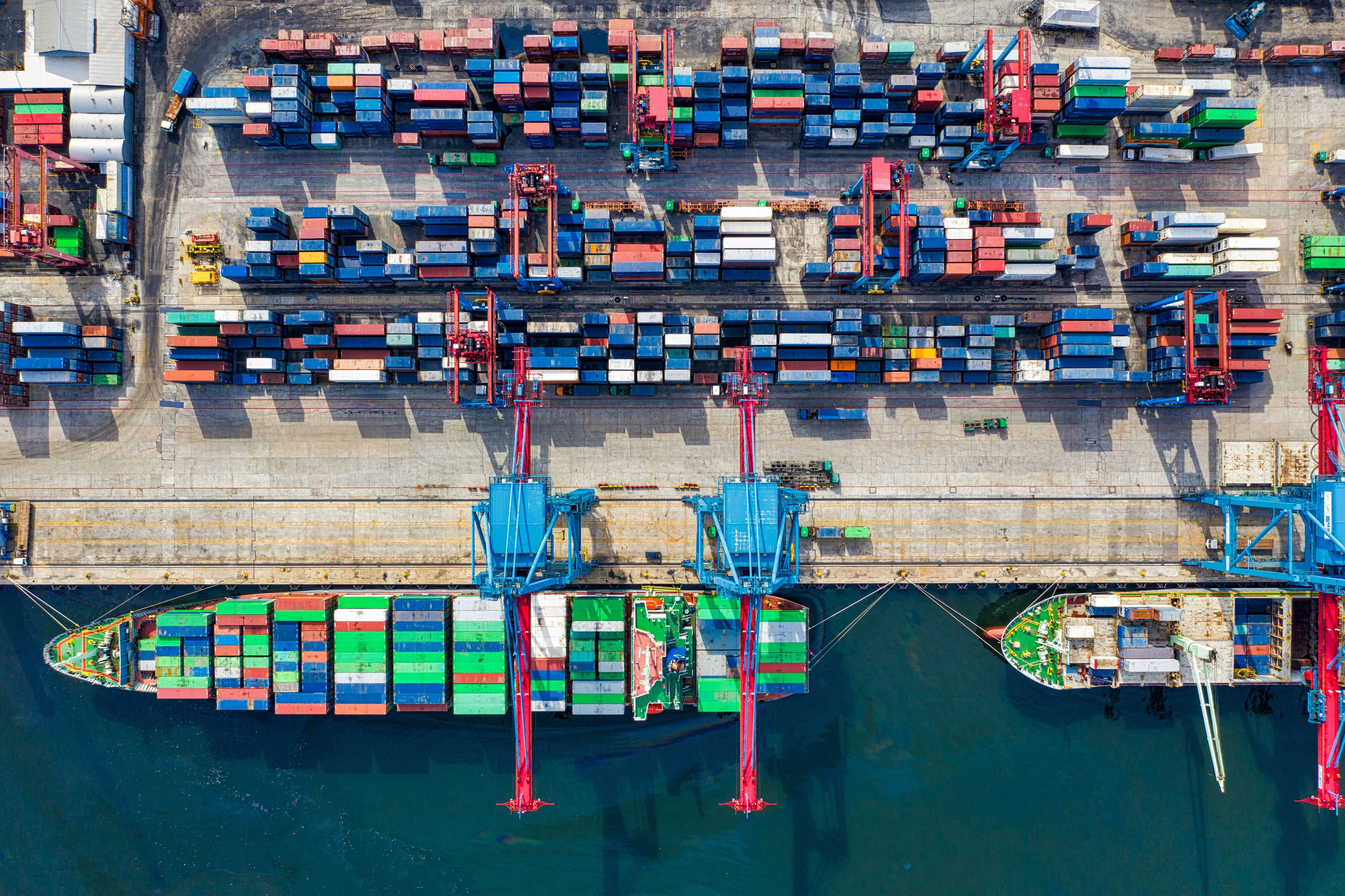 Porto visto dall'alto: file di container colorati, gru e navi in banchina