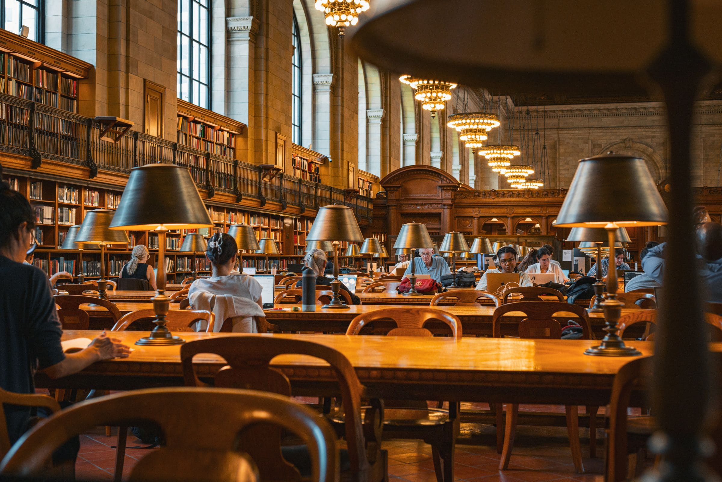 Sala di lettura di una grande biblioteca, con lampade accese sui tavoli