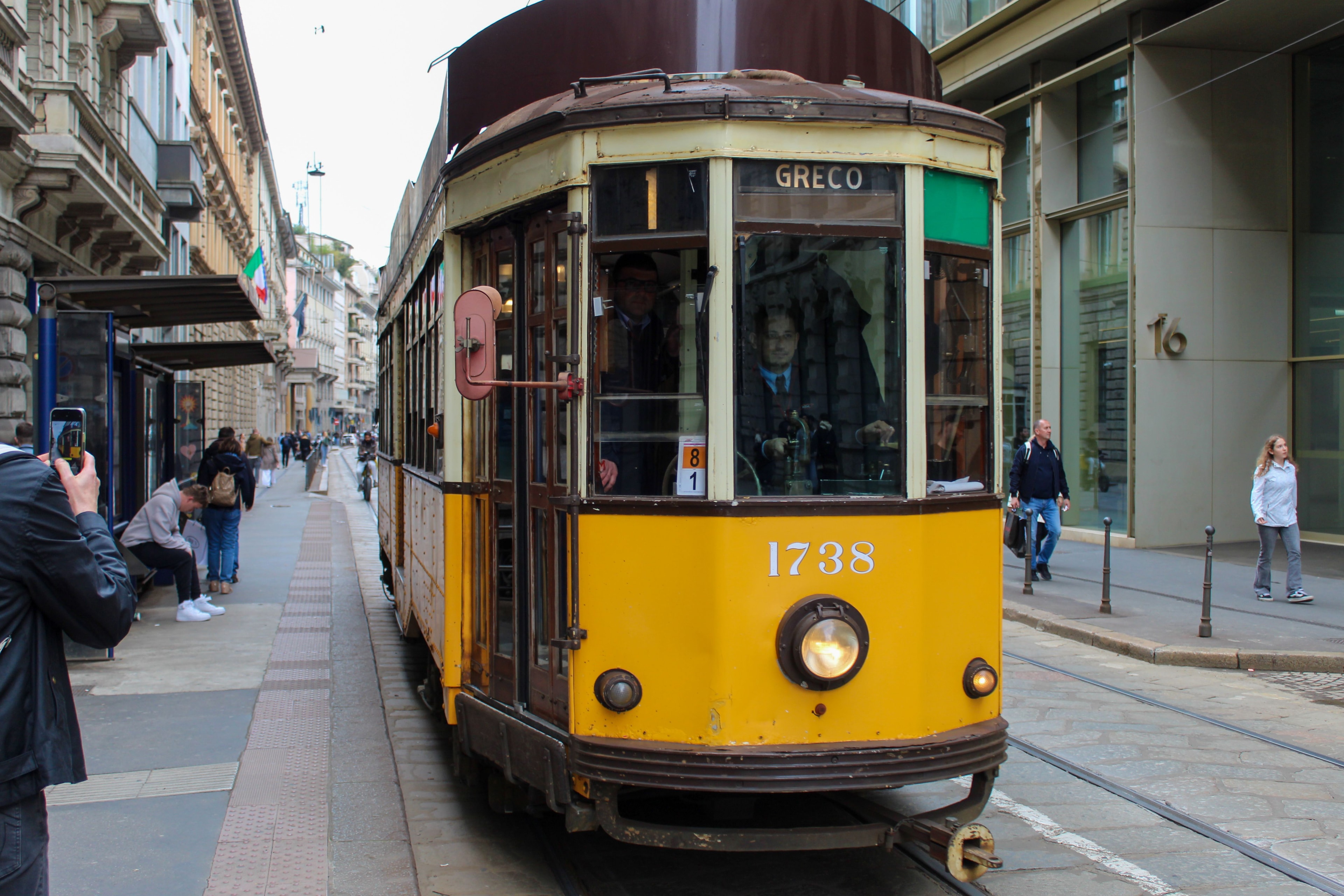 Tram storico giallo in una via di Milano, con il tricolore sullo sfondo